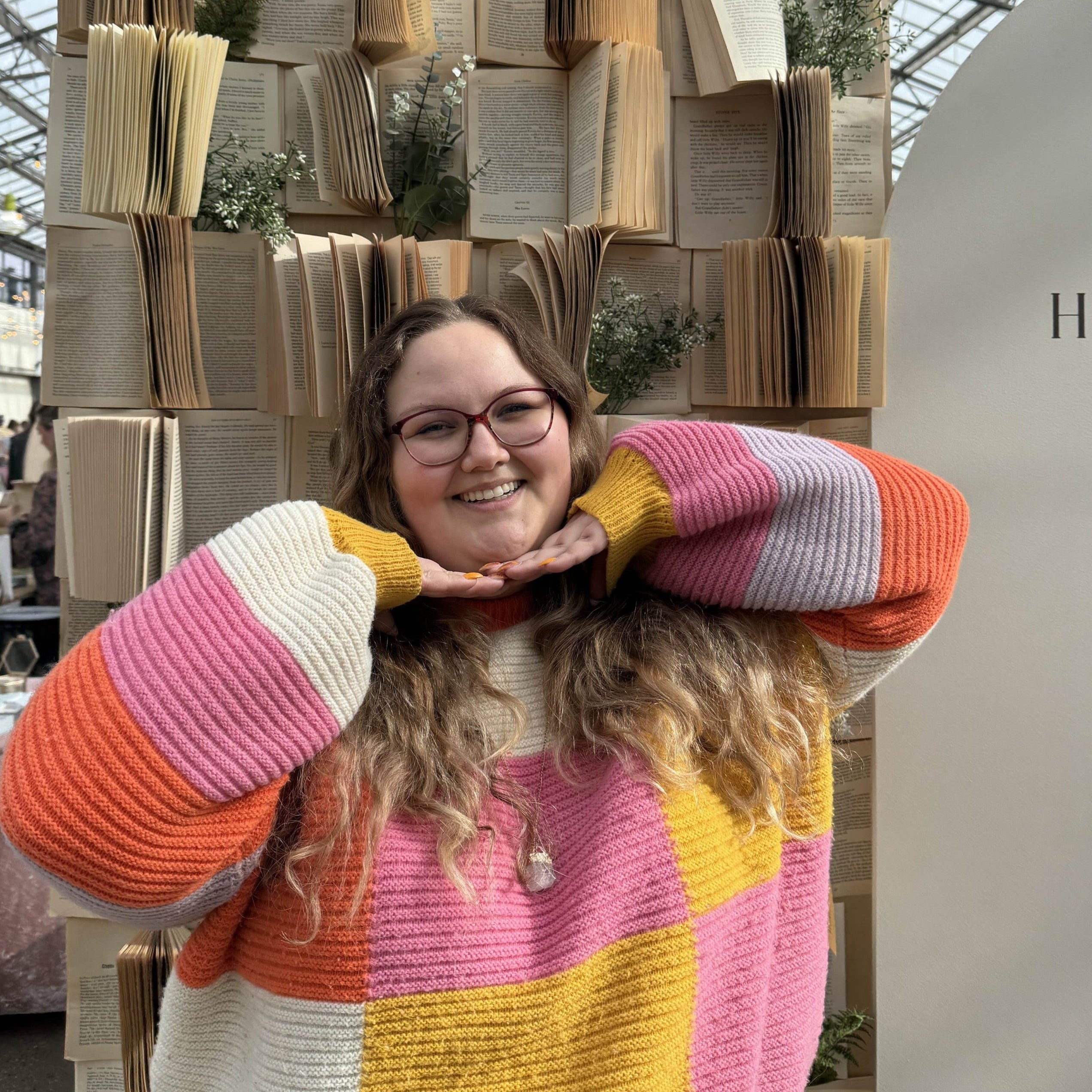Victoria wearing a colorful sweater standing in front of a book sculpture with a modern indoor setting.