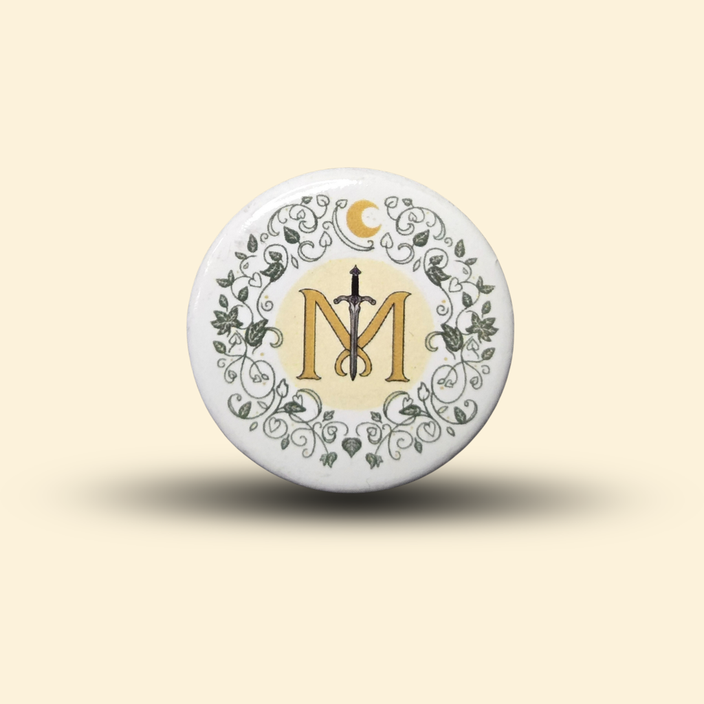 Mythic Manuscripts logo button pin featuring a gold 'M' overlaid by a sword, framed by a floral wreath.