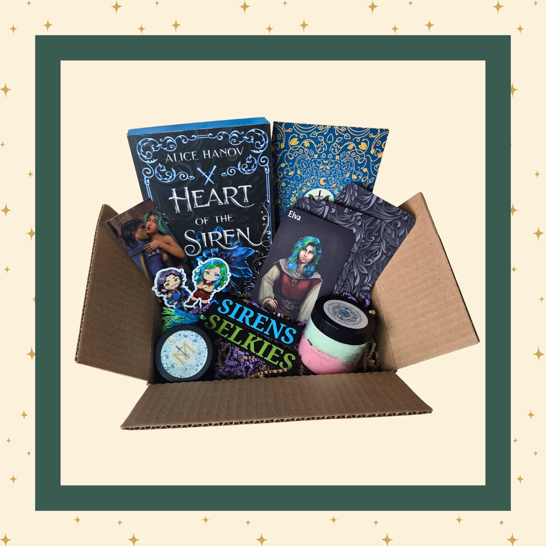 An open gift box containing a curated selection of items: a blue and black covered book titled "Heart of the Siren," art featuring the main characters of the book, a round candle container with a stylized "M" label, a multicoloured sugar scrub, several themed stickers, and additional small items.