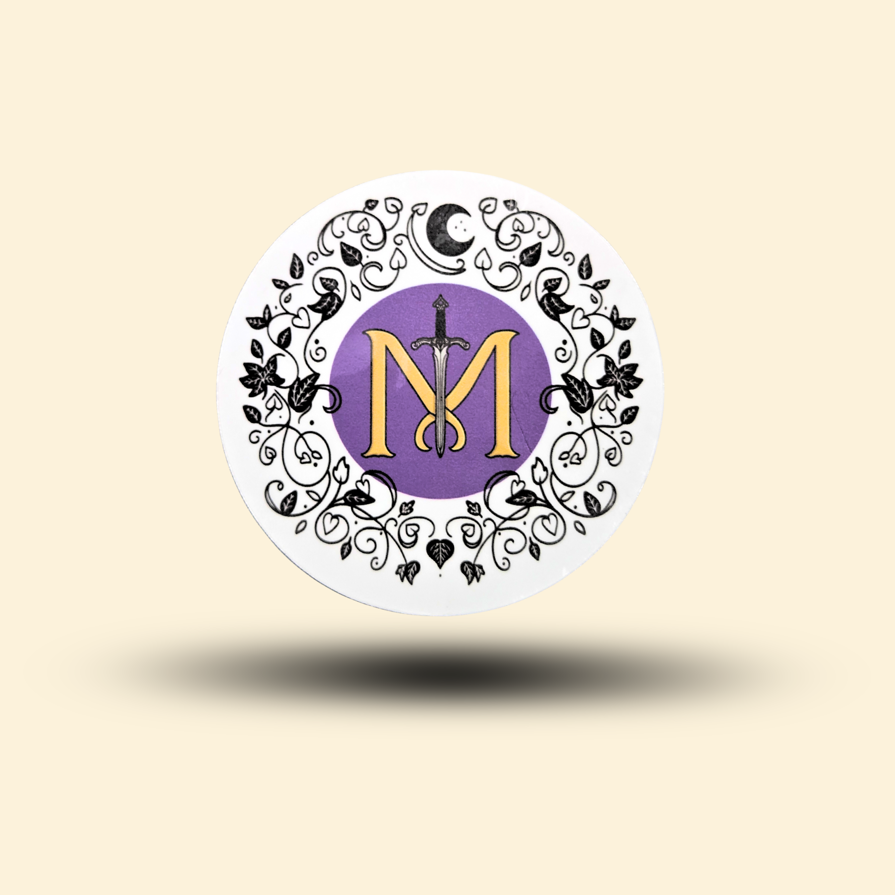 Mythic Manuscripts store logo sticker with a gold "MM" and a fantasy sword set in a purple circle and framed by a black floral wreath.